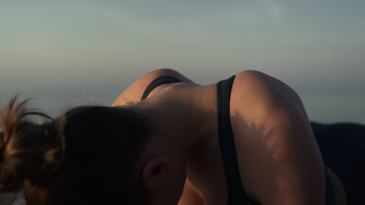 chica relajada doblando el cuello de pie en una postura de tabla en la playa de cerca. mujer estirándose
