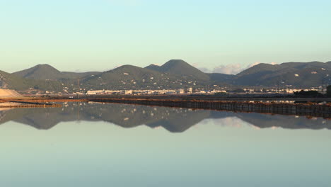 left pan de las salinas de ibiza with the dawn lights reflected in the water, in the background the quarry of ibiza, spain