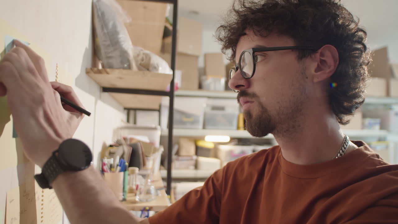 Man Writing Tasks on Paper Attached to Wall in Workshop