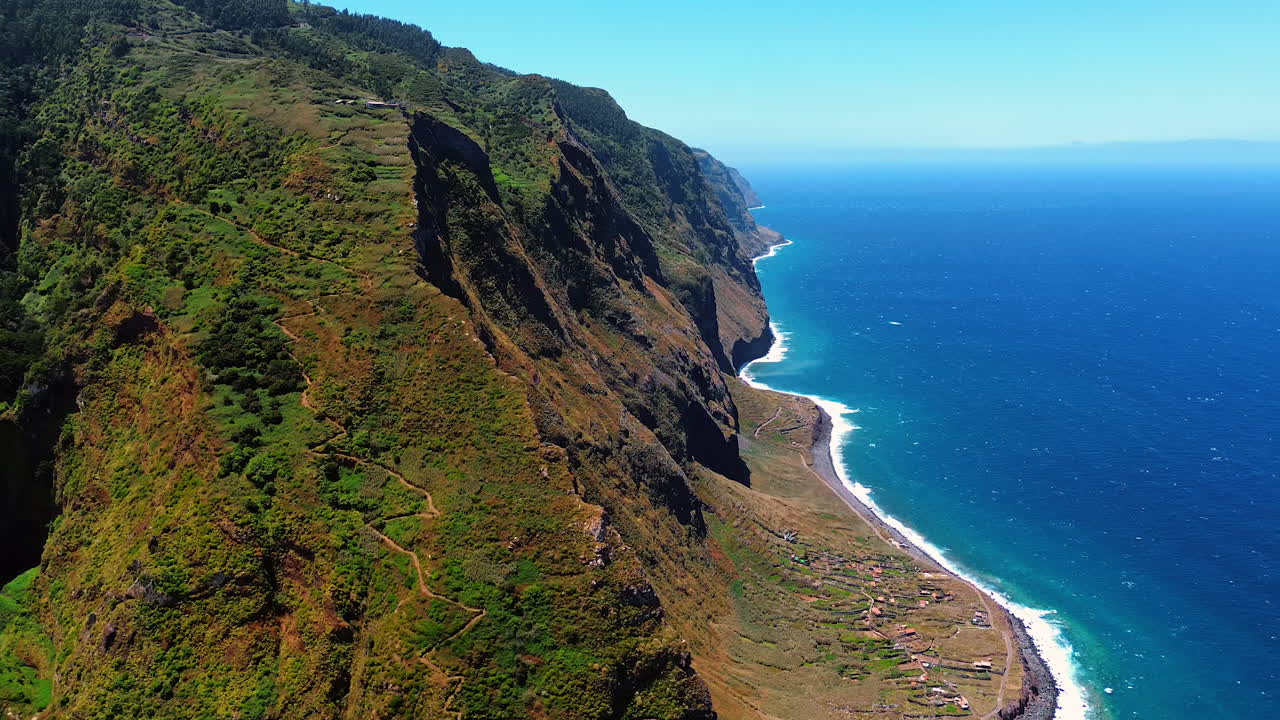 Wavy touristic path crosses the slope of a huge mountain at the coast of the Atlantic Ocean. Stunning view of the rocky coast of the Madeira Islands, Portugal. Top view.