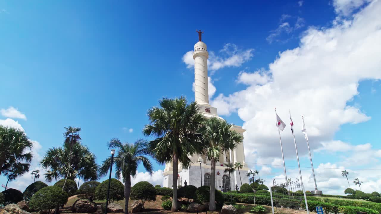 Carrellata dal basso attraverso le palme che rivela il Monumento a los Heroes de la Restauración sotto un cielo blu con nuvole a Santiago, Repubblica Dominicana.