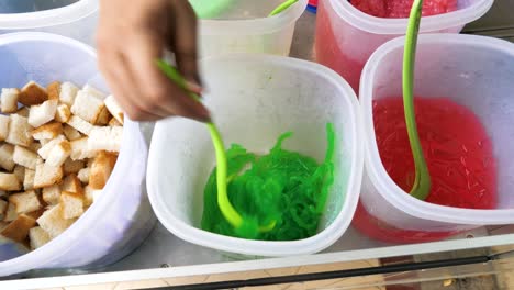 slow motion shot of a street vendor scooping pandan jelly for the famous es campur snack, indonesia