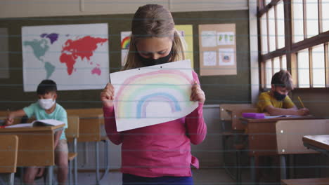 school concept icons over girl wearing face mask holding a rainbow painting at elementary school