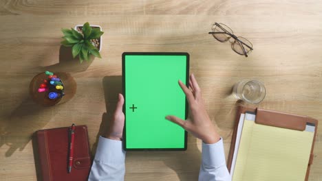 vista de arriba hacia abajo de una computadora portátil con pantalla verde simulada pantalla chromakey en un escritorio de oficina de madera al lado de la libreta con bolígrafos, gafas y un vaso de agua.