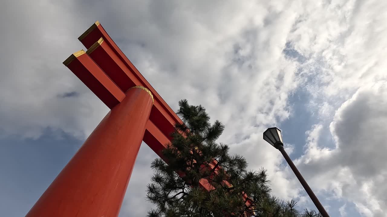 Looking Up at Massive Vermilion Torii Gate with Gold Accents Under Cloudy Sky at Heian Shrine Entrance in Kyoto, Japan