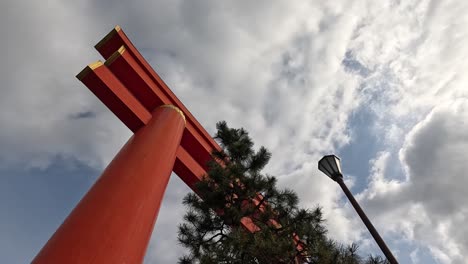 looking up at massive vermilion torii gate with gold accents under cloudy sky at heian shrine entrance in kyoto, japan