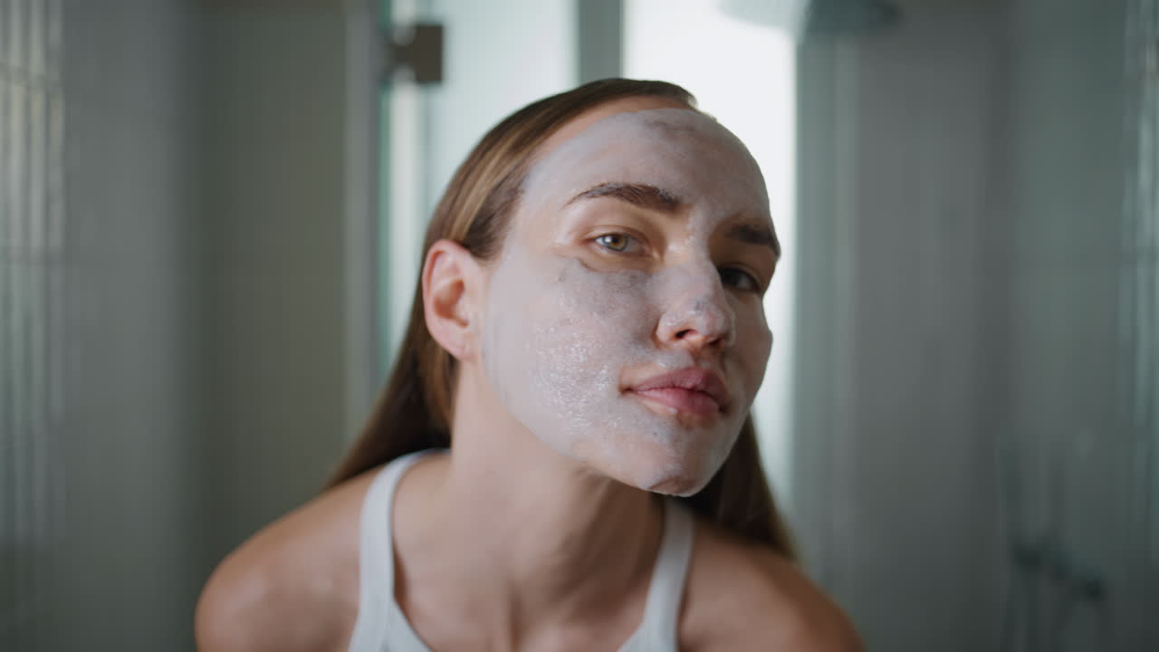 Girl wearing facial mask in bathroom closeup. Pretty model moisturizing skin