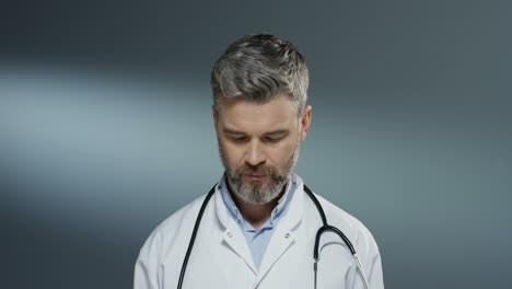 portrait shot of the good looking man physician in white gown and with stethoscope on his neck rising face up and smiling to the camera