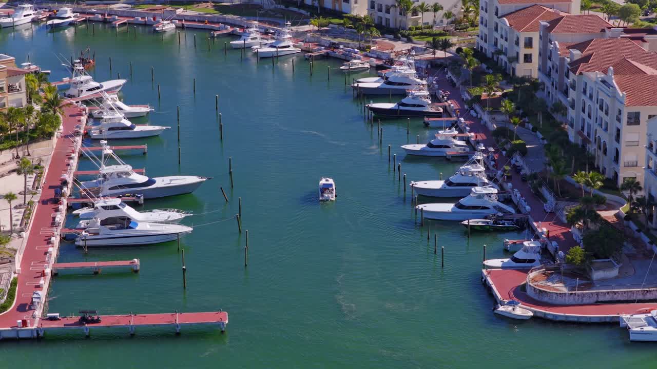 Barca di lusso che arriva al porto turistico di Cap Cana, circondata da residenze di lusso sul lungomare, banchine fiancheggiate da palme e calme acque turchesi nella Repubblica Dominicana. Giornata di sole in estate. Vista aerea