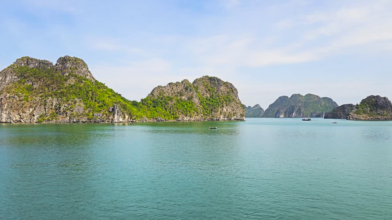 Majestic limestone karsts rise dramatically from the tranquil turquoise waters of Ha Long Bay, creating a mesmerizing seascape where scattered boats navigate through the mystical formations