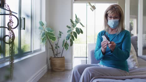 senior woman wearing face mask wiping her smartphone with a tissue