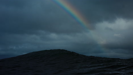 Rainbow-arches-across-grey-stormy-sky-view-from-back-of-wave-in-cold-water