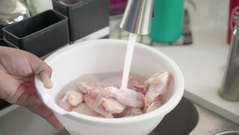 la mano del hombre abre el grifo para dejar correr el agua sobre el pollo crudo