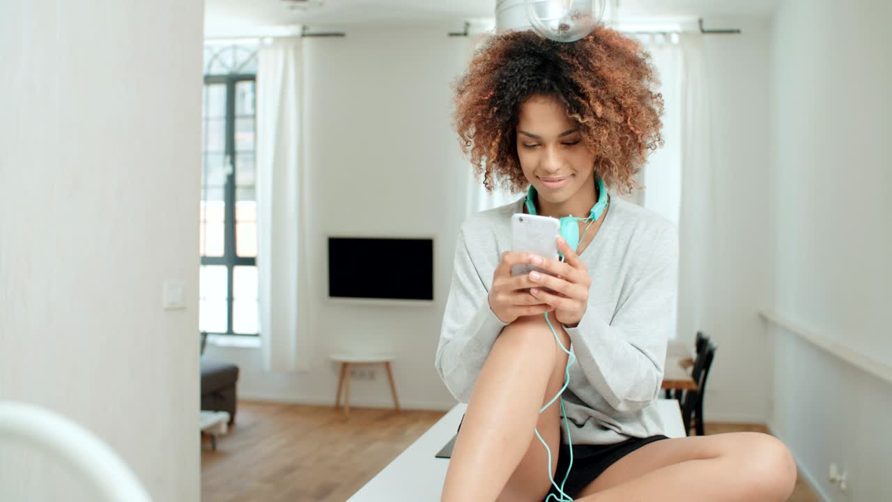 una hermosa joven afroamericana enviando mensajes de texto por teléfono móvil en casa.