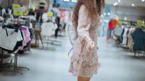 mujer sonriente en vestido vintage baila felizmente en una tienda de ropa iluminada, expresando alegría y emoción, otros compradores son visibles en el fondo