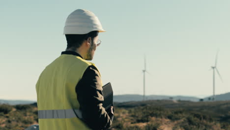A-male-professional-engineer-in-reflective-gear-audits-wind-turbines-while-walking,-highlighting-the-importance-of-maintenance-for-eco-friendly-energy