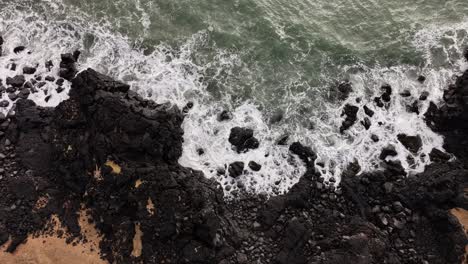 top-down aerial view of waves crashing against the rugged shores near búðakirkja in búðir, snæfellsnes peninsula, iceland, capturing raw coastal energy in winter tones.