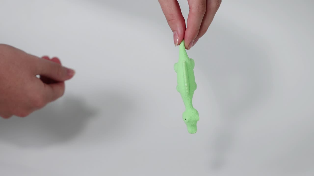 manos estirando un juguete de dinosaurio verde