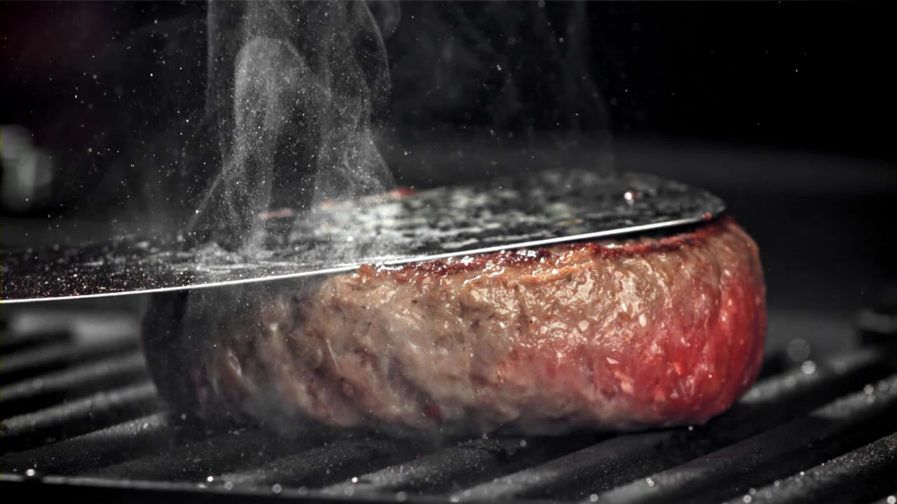 Dampende burgerbøf bliver presset på en varm grill.