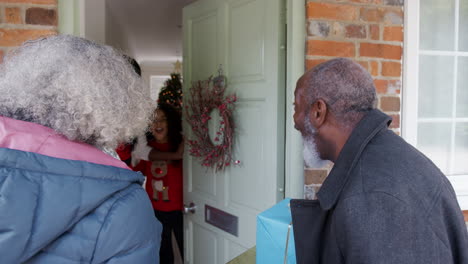 Grandparents-Being-Greeted-By-Mother-And-Daughter-As-They-Arrive-For-Visit-On-Christmas-Day-With-Gifts