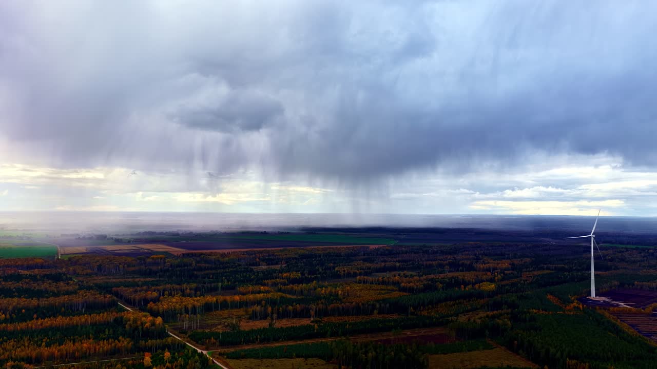 Regnbyge falder over tæt skov, drone filmer vindmølle på store marker i Letland.