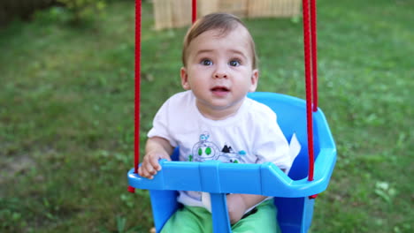 baby boy swaying in the swing hanging in the garden. spending summer in the nature. view from above. blurred backdrop.