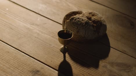 concepto religioso filmado con pan de cáliz y vino en una mesa de madera con un charco de luz 6