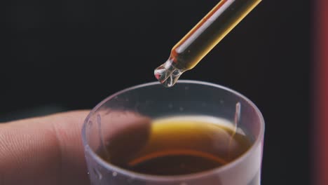 person puts pipette into brown liquid on dark background