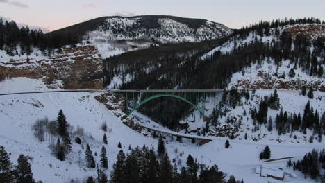 Aerial-Cinematic-drone-Vail-Avon-Red-Cliff-Iconic-Colorado-Bridge-mid-winter-cars-driving-in-snow-late-sunset-pan-reveal-backwards-movement