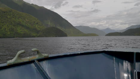 slow motion pan across bow of a boat in doubtful sound fjord with mountains and water - patea, new zealand