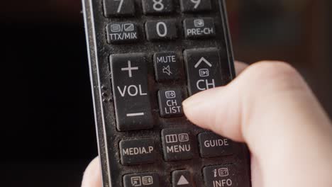 person pressing remote control television volume button