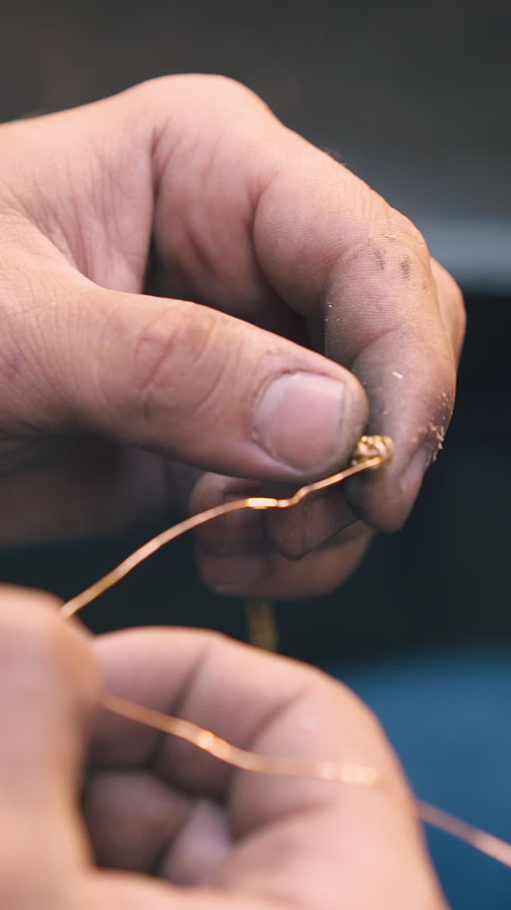 CU shot: professional jeweler twists golden wire connected to new shining bracelet in light workshop close view