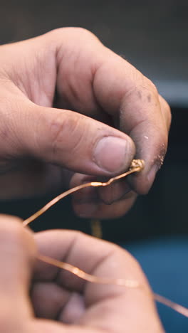 cu shot: professional jeweler twists golden wire connected to new shining bracelet in light workshop close view