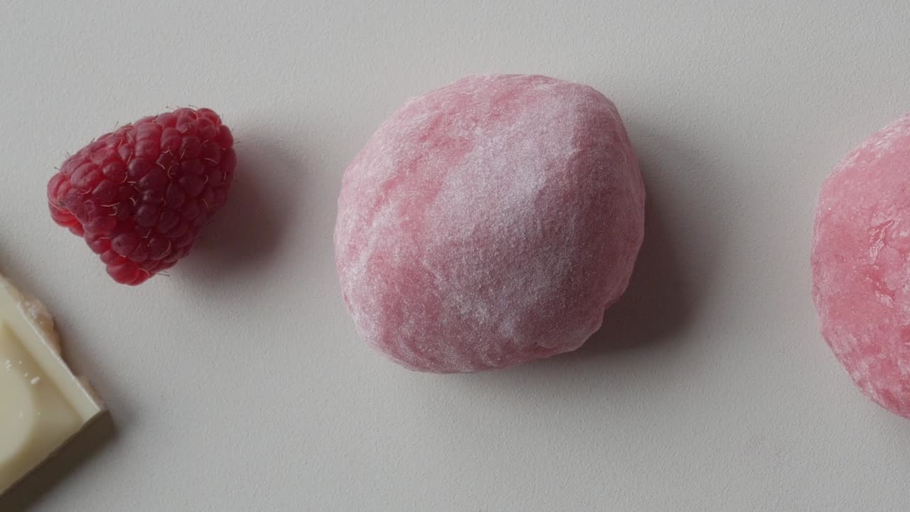 Close-up of two strawberry mochi balls next to raspberry and white chocolate pieces