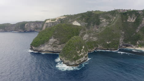 slow pivot aerial shot around a peninsula at kelingking beach with steep cliffs  on a cloudy day, nusa penida, bali, indonesia.