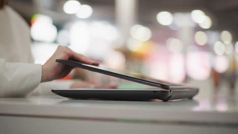 close-up of hand reaching to open a closed laptop on a sleek white table in a modern indoor environment, vibrant blurred bokeh lighting