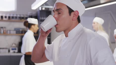Mixed-race-male-chef-wearing-chefs-whites-in-a-restaurant-kitchen-holding-a-mug-and-drinking