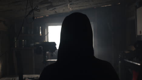 hooded person walks into metal workshop from behind