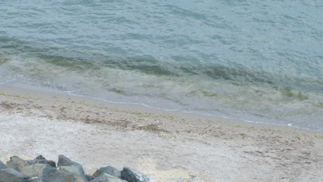 Turquoise-Sea-Waves-Rolling-on-Empty-Beach-Nearby-Coastal-Rocks,-4K