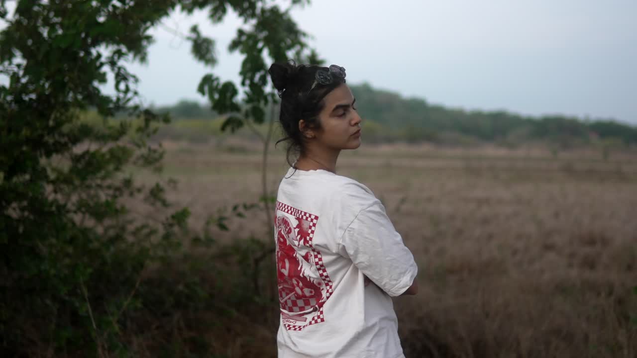 셔츠를 입은 여자가 잔디에 서서 구름이 많은 날 카메라를 돌아보고 있다.