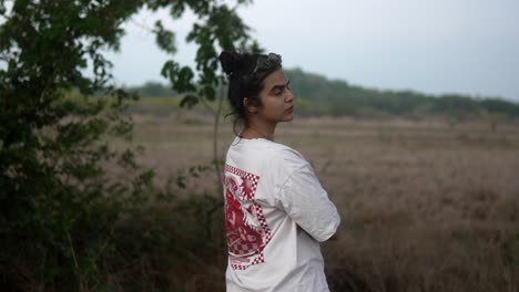 Woman-in-a-white-shirt-stands-in-a-grassy-field-looking-back-at-the-camera-on-a-cloudy-day