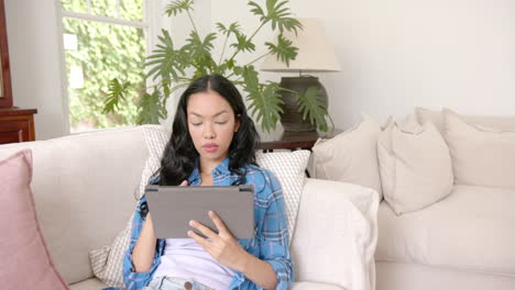 young biracial woman with long black hair holds a tablet, smiling at camera