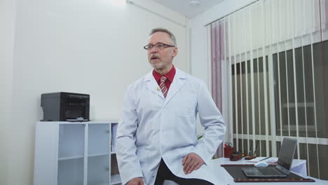 smiling doctor sitting at his desk in his office. doctor is working in his medical office