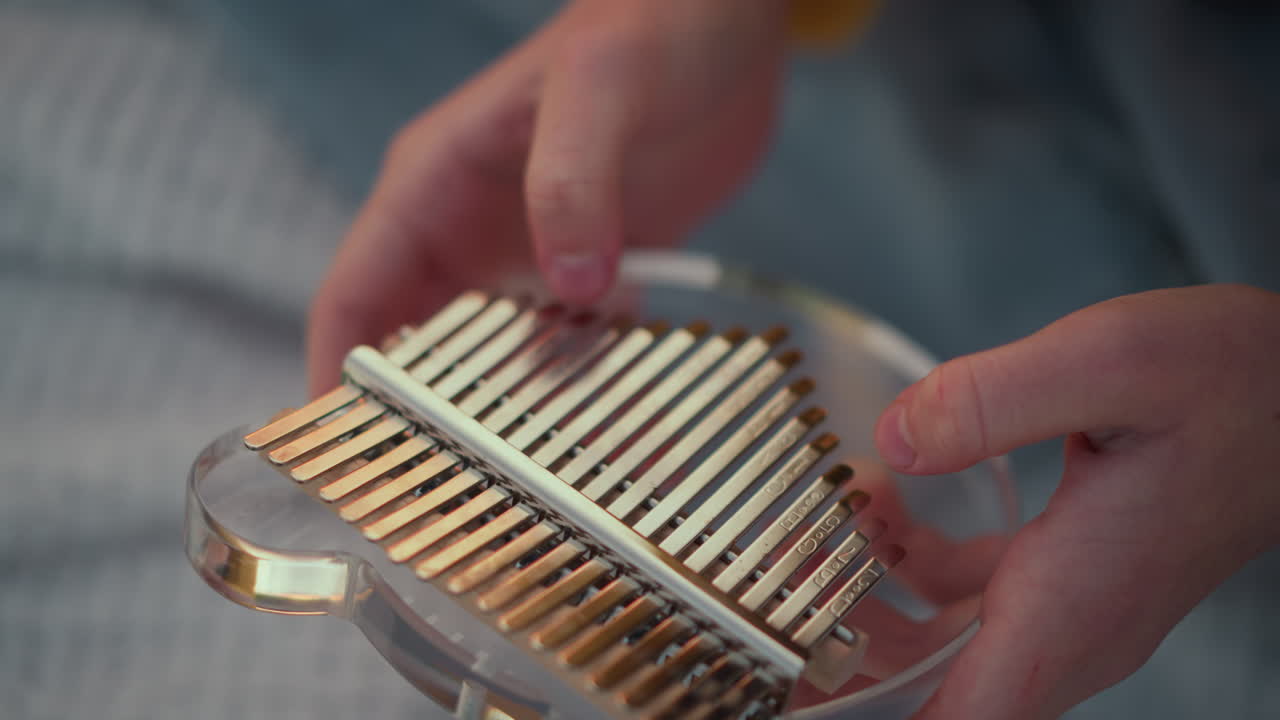 closeup fingers playing kalimba indoors on blanket, student practices scales and finger techniques under lamp, warm evening ambiance, tactile plucks and soft resonance, focused cozy session