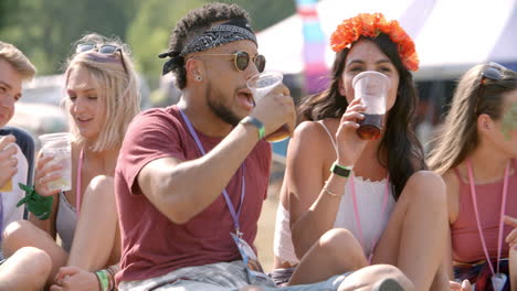 friends sit on grass talking at a music festival, front view