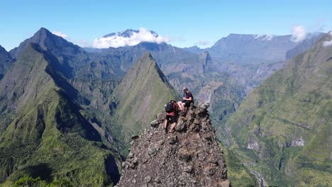 drone footage of two people climing steep rock in front a scenery of the cirque of mafate at the reunion island