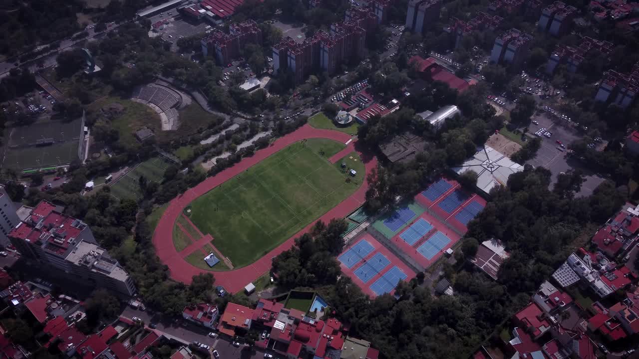 toma de un campo deportivo con canchas de tenis, pista de atletismo, campos de fútbol, al sur de la ciudad de méxico, el complejo está rodeado de edificios residenciales con techos rojos