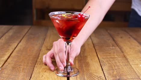 waiter rotating a red fruit cocktail on a wooden table