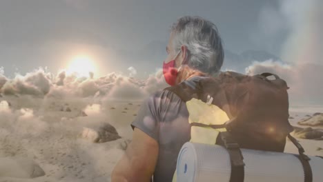 hombre mayor caucásico con máscara facial caminando por la costa, sobre nubes que se mueven rápidamente
