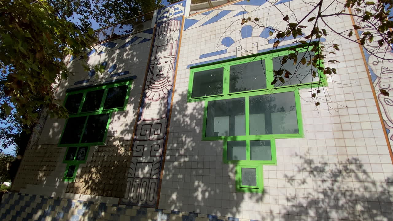 Pabellón temático de Guatemala en Sevilla cubierto de azulejos azules y blancos con aves tropicales y patrones culturales rodeado de árboles centenarios